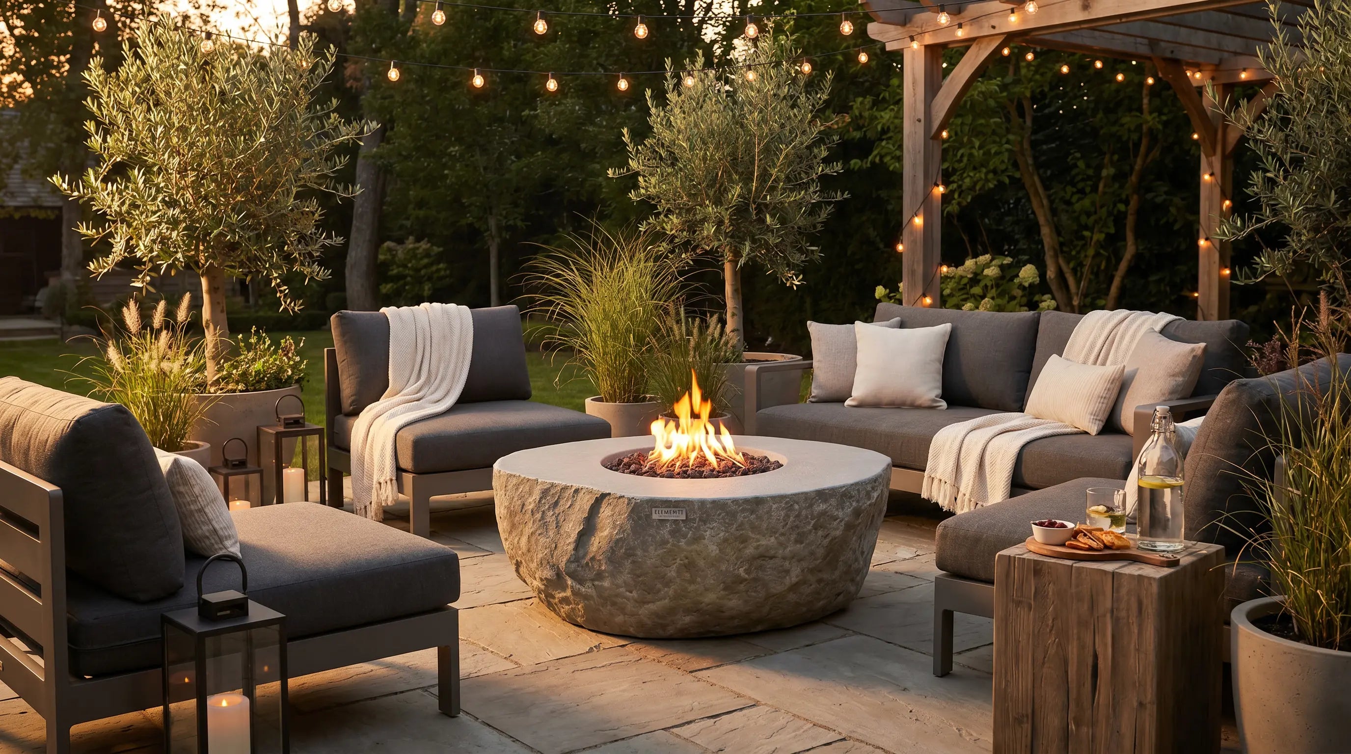 Elementi Boulder round concrete gas fire table glowing on a patio at dusk