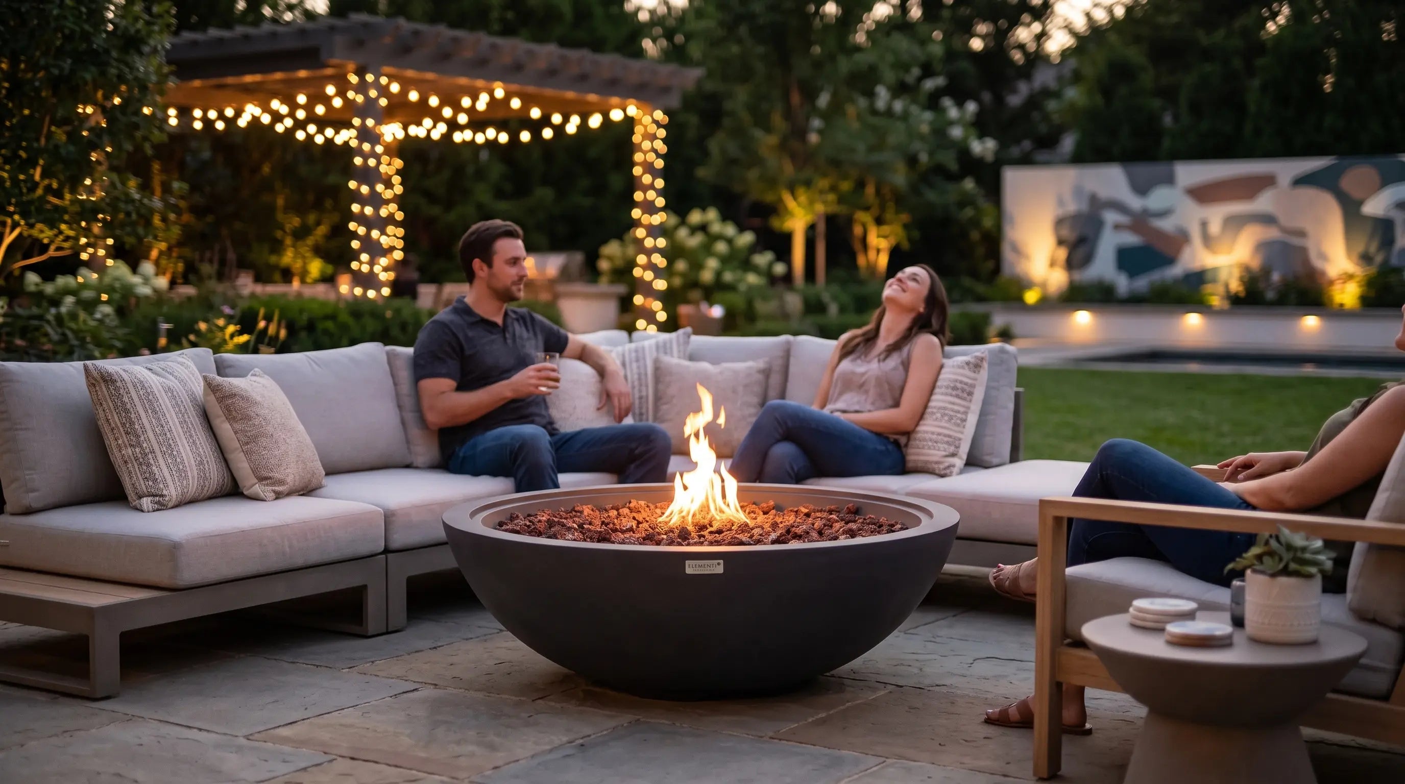 Round concrete gas fire bowl as the centerpiece of a patio lounge at dusk