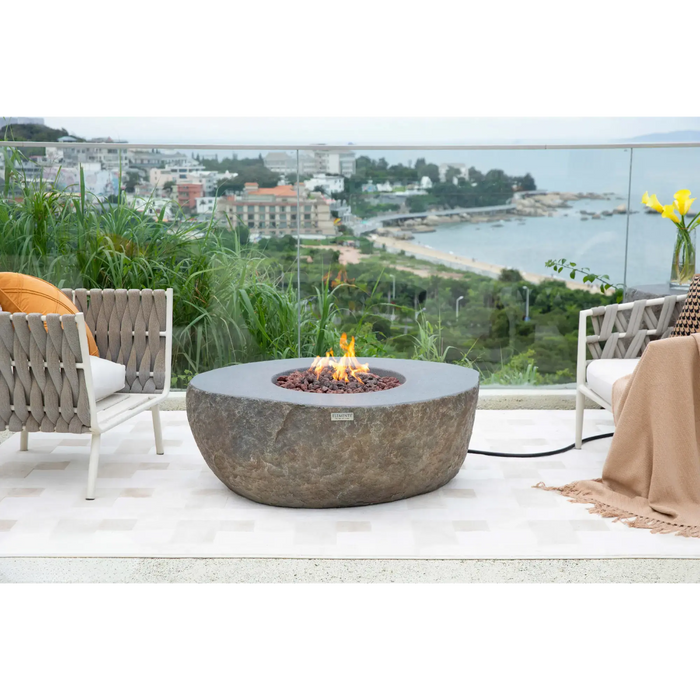 Elementi Boulder round fire pit table in lifestyle outdoor setting — sculptural natural stone-style concrete fire pit