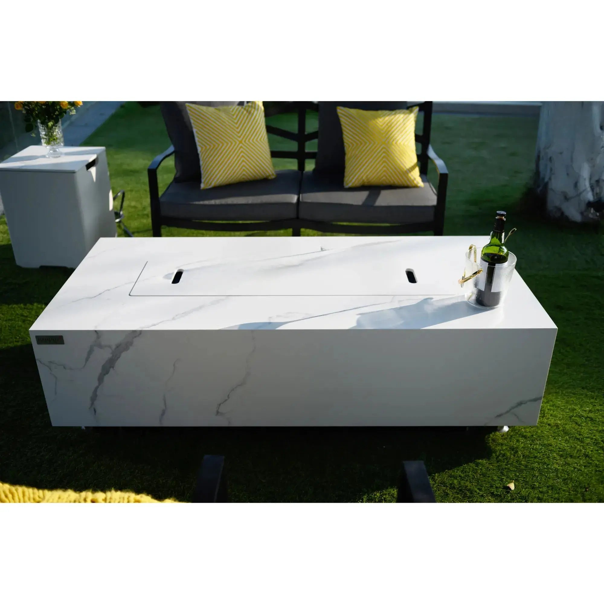 White outdoor fire pit table with a bottle on a grassy area